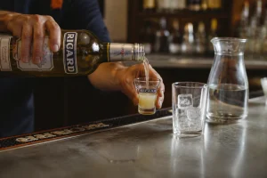 Un serveur verse une dose de Ricard de 2 cl dans une mezurette au comptoir d'un bar français