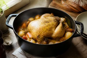 Poularde dorée mijotant en cocotte en fonte avec légumes, recette grand-mère