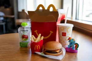 Boîte Happy Meal ouverte avec burger, frites, dessert fruité, boisson et jouet sur une table